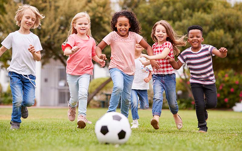 Group Of Children Playing soccer With Friends In Park