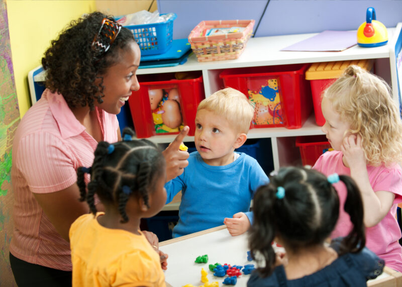 Teacher with four toddlers in a bright, colorful classroom.