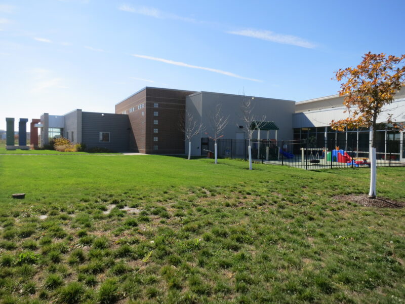 Back of KidsPoint C Street building with green grass, tree, and enclosed playground.