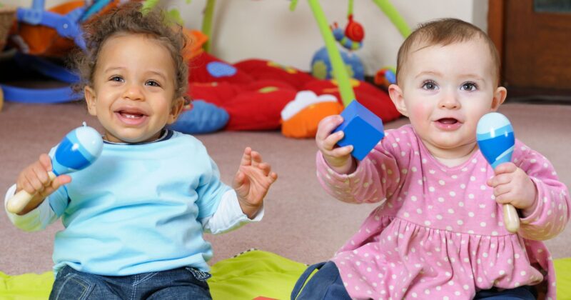 Two older babies sitting up holding musical shakers.
