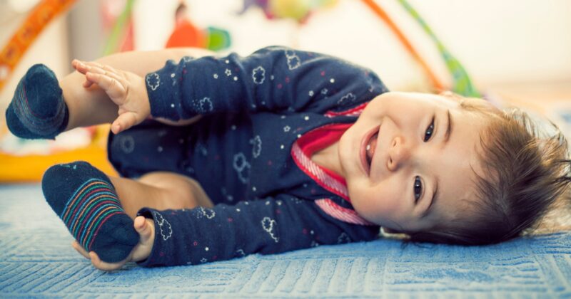 A cute baby laying on its side holding its feet near a play gym.