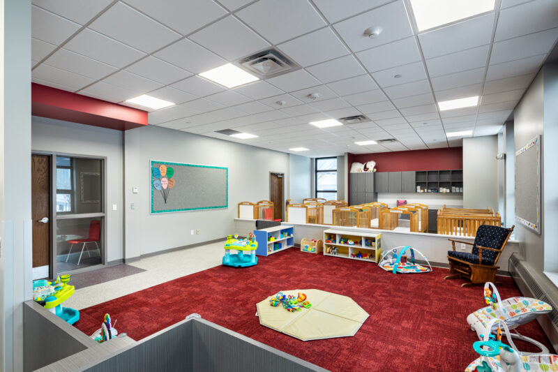 Baby room with red rug and accents and playmat and baby toys.