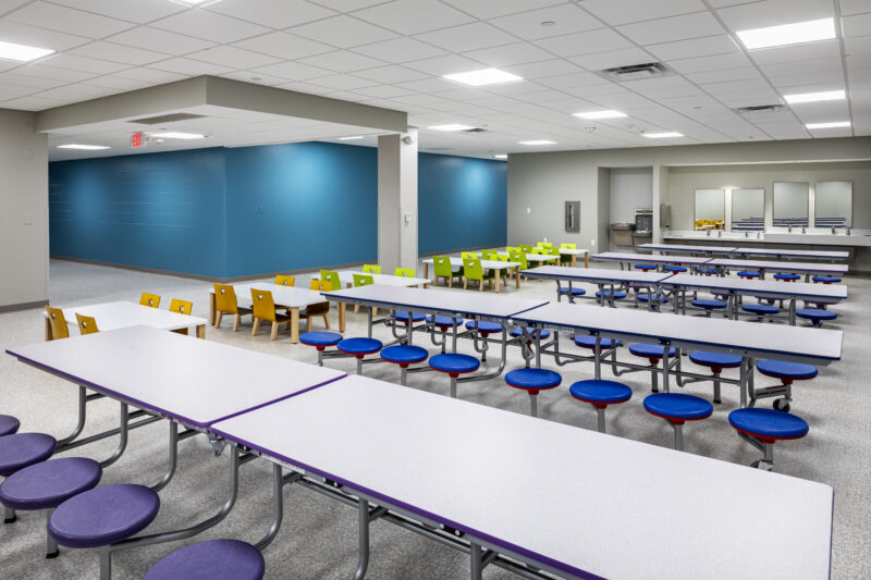 Bright, clean children's cafeteria with long tables and stools and chairs.