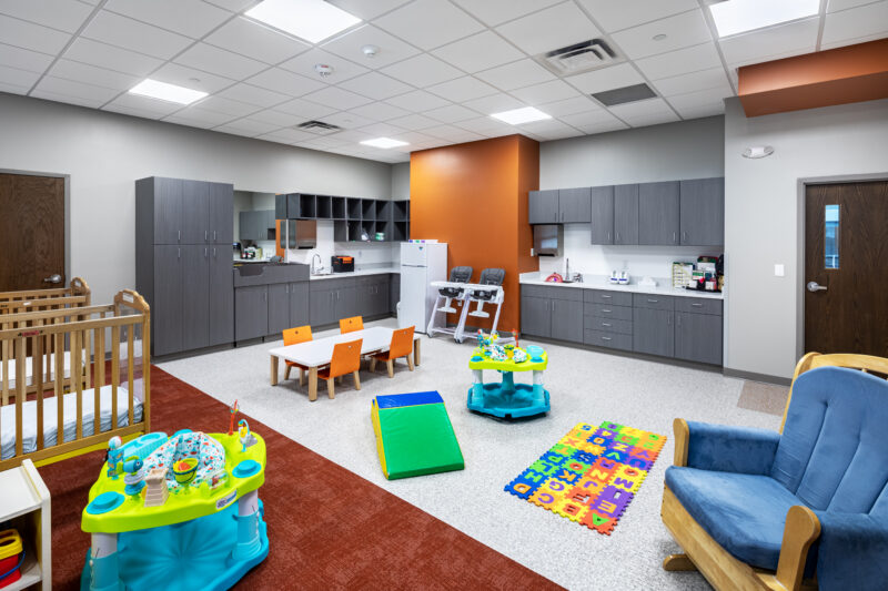 Infant Room with orange run and accents, tables and chairs, and baby toys.