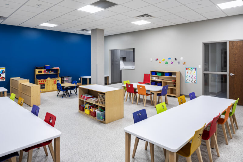 Colorful preschool room with blue accent wall and tables and colorful chairs.